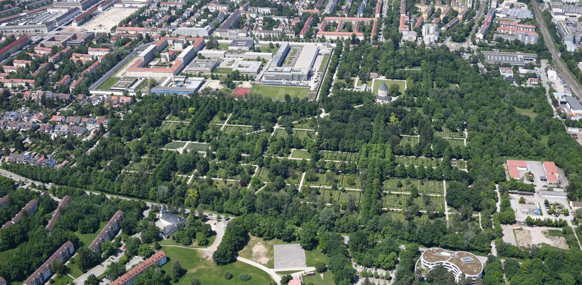 Luftbild des Friedhofs am Perlacher Forst mit Trauerhalle, Wegen und dichtem Baumbestand